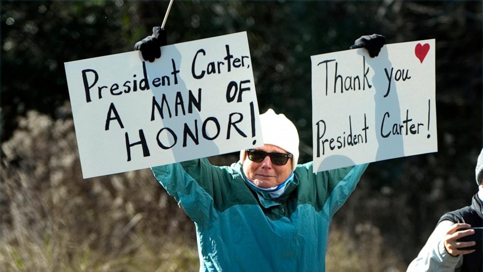 PHOTO: A person holds signs as the hearse containing the casket of former President Jimmy Carter, pauses at the Carter boyhood farm on Jan. 4, 2025, in Archery, Georgia.