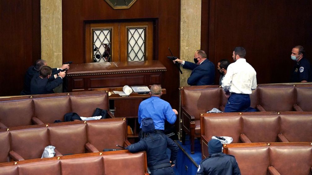 PHOTO: Law enforcement officers point their guns at a door that was vandalized in the House Chamber during a joint session of Congress on Jan. 6, 2021, in Washington, D.C. 