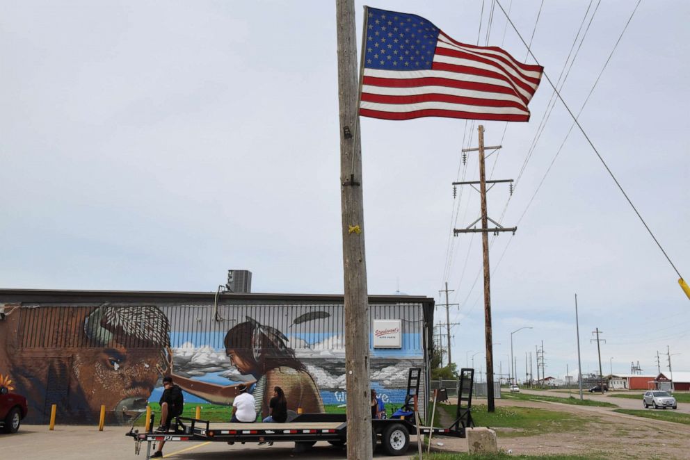 PHOTO: People sit in front of a mural depicting a buffalo and a Native American man along the main road on the Cheyenne River Reservation in Eagle Butte, S.D., May 28, 2018.