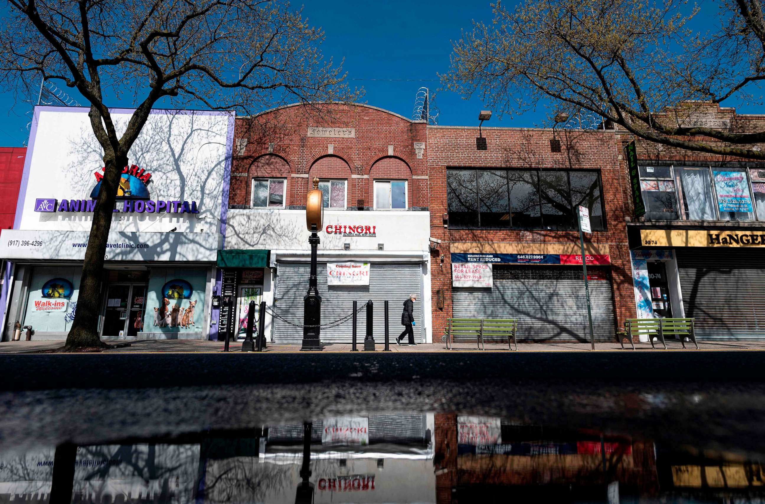 PHOTO: A woman wearing a mask walks past closed store fronts in the Astoria neighborhood of Queens in New York, April 15, 2020.