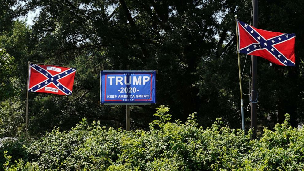 PHOTO: A campaign sign for U.S. President Donald Trump sits between two Confederate flags, one bearing the words "I ain't coming down" in the backyard of a home in Sandston, Va., July 4, 2020. 