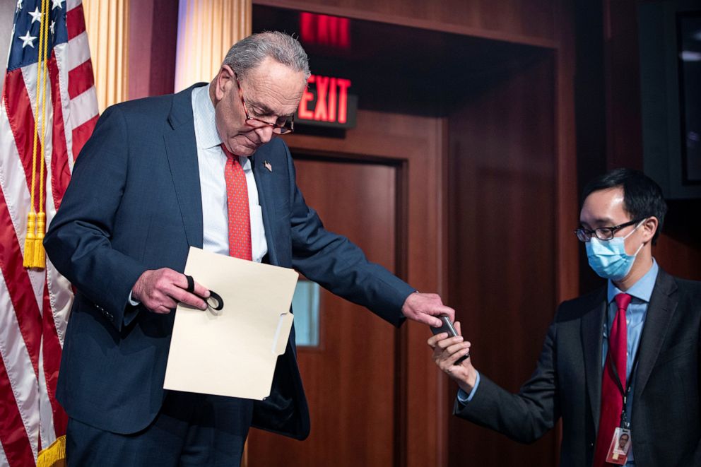 PHOTO: Senate Minority Leader Chuck Schumer hands his cell phone to an aide during a weekly news conference in Washington,Dec. 15, 2020.