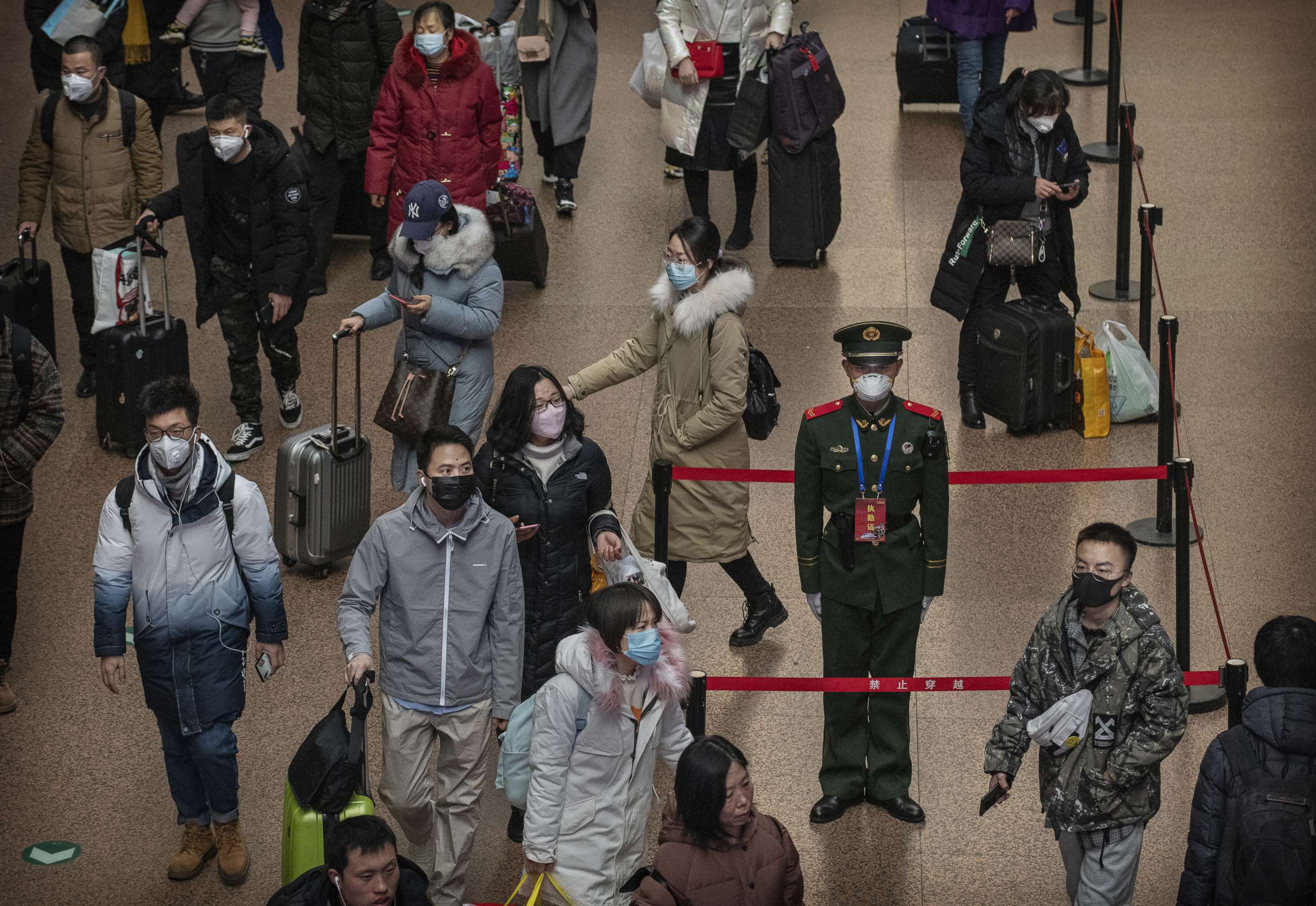 PHOTO: A Chinese police officer wears a protective mask as passengers, many wearing masks also, arrive to board trains before the annual Spring Festival at a Beijing railway station in Beijing, Jan. 23, 2020.