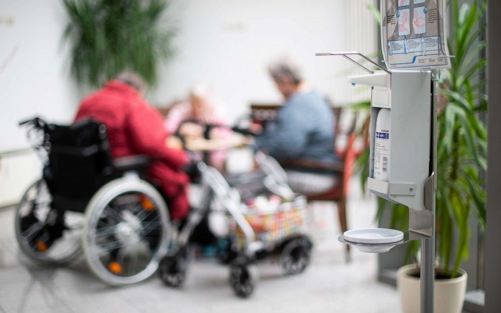 PHOTO: A disinfectant dispenser hangs in a nursing home in Germany while senior citizens play in the background, March 13, 2020.