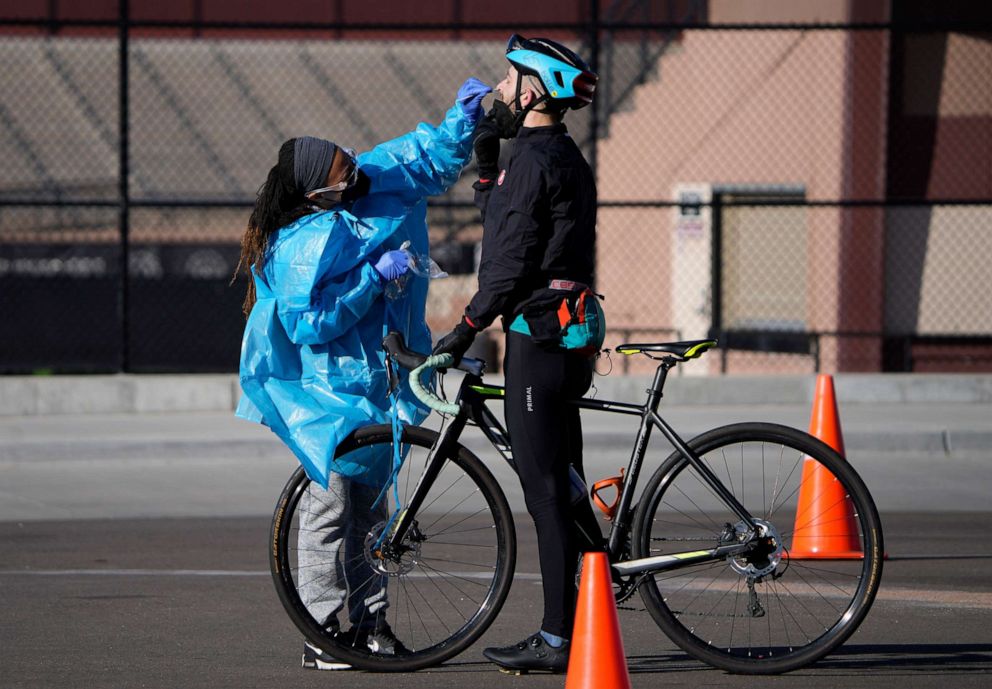 PHOTO: A medical technician performs a nasal swab test on a cyclist queued up in a line with motorists at a COVID-19 testing site near All City Stadium, Dec. 30, 2021, in Denver.