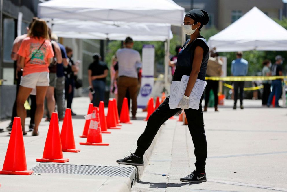 PHOTO: Medical assistant Jasmine Lyons provides paperwork to persons in line at a walk up COVID-19 test site in Dallas, June 11, 2020.