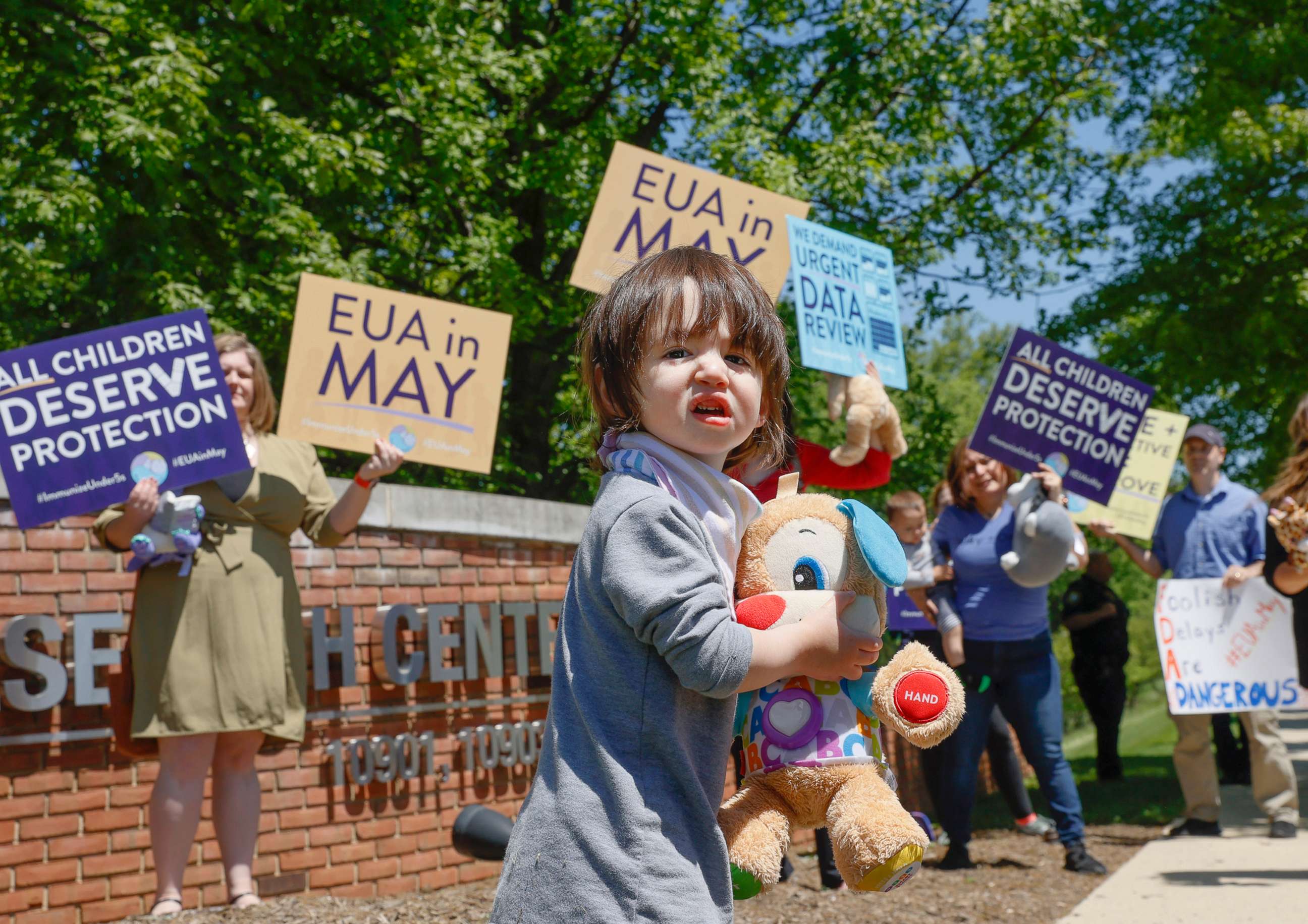 PHOTO: A child walks in front of demonstrators holding up signs urging the Food and Drug Administration to authorize vaccines for children under 5 at the FDA on May 9, 2022 in Washington, D.C.
