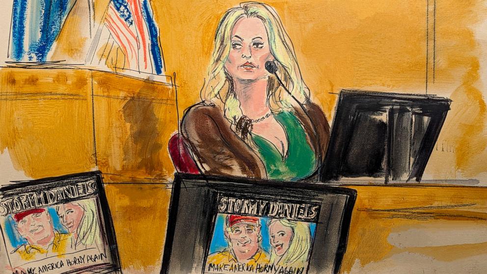 PHOTO: Stormy Daniels testifies on the witness stand as a promotional image for one of her shows featuring an image of Trump is displayed on monitors in Manhattan criminal court, May 9, 2024, in New York.