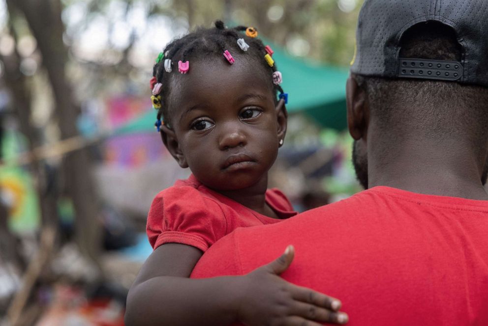PHOTO: A Haitian father carries his daughter through the large migrant camp near an international bridge at the U.S.-Mexico border, Sept. 21, 2021, in Del Rio, Texas.