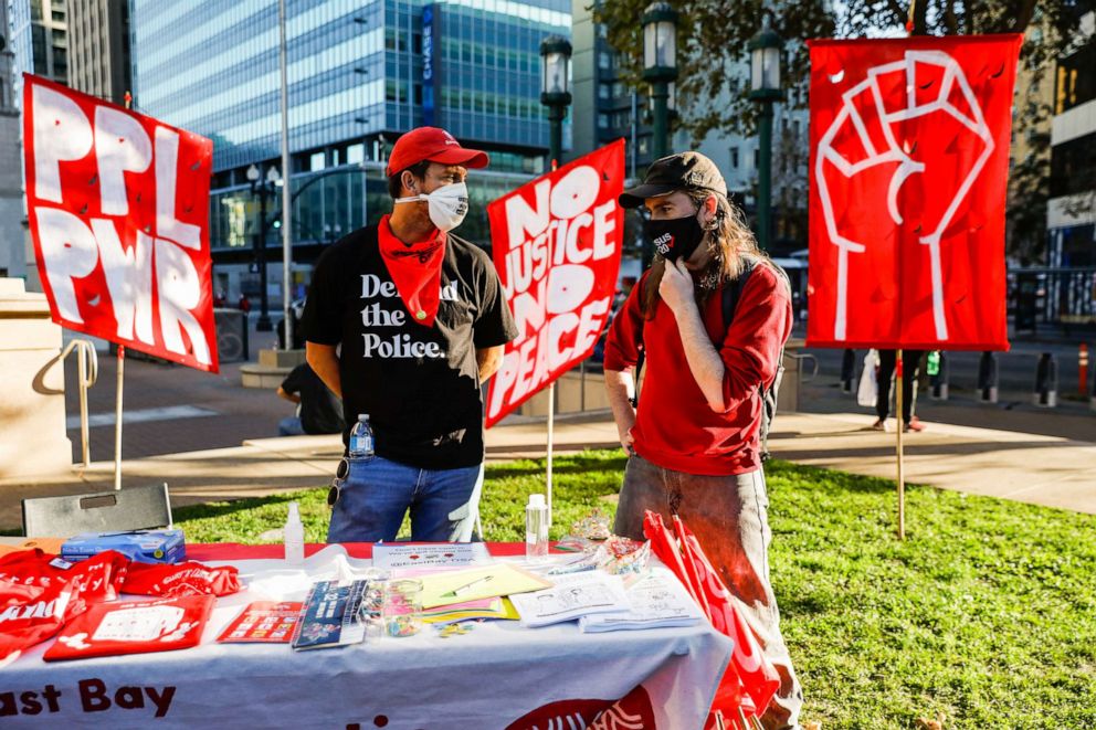 PHOTO: AJ Acosta and Will Shattuc chat behind the East Bay Democratic Socialists of America table during the Defend Our Democracy: Count Every Vote event held at Frank Ogawa Plaza in Oakland, Calif., Nov. 4, 2020.