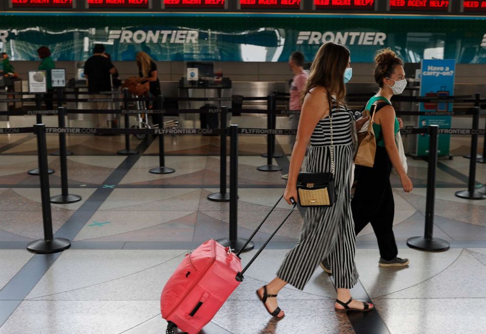 PHOTO: A pair of masked travelers head to the ticketing counter for Frontier Airlines in the main terminal of Denver International Airport in Denver, July 22, 2020.