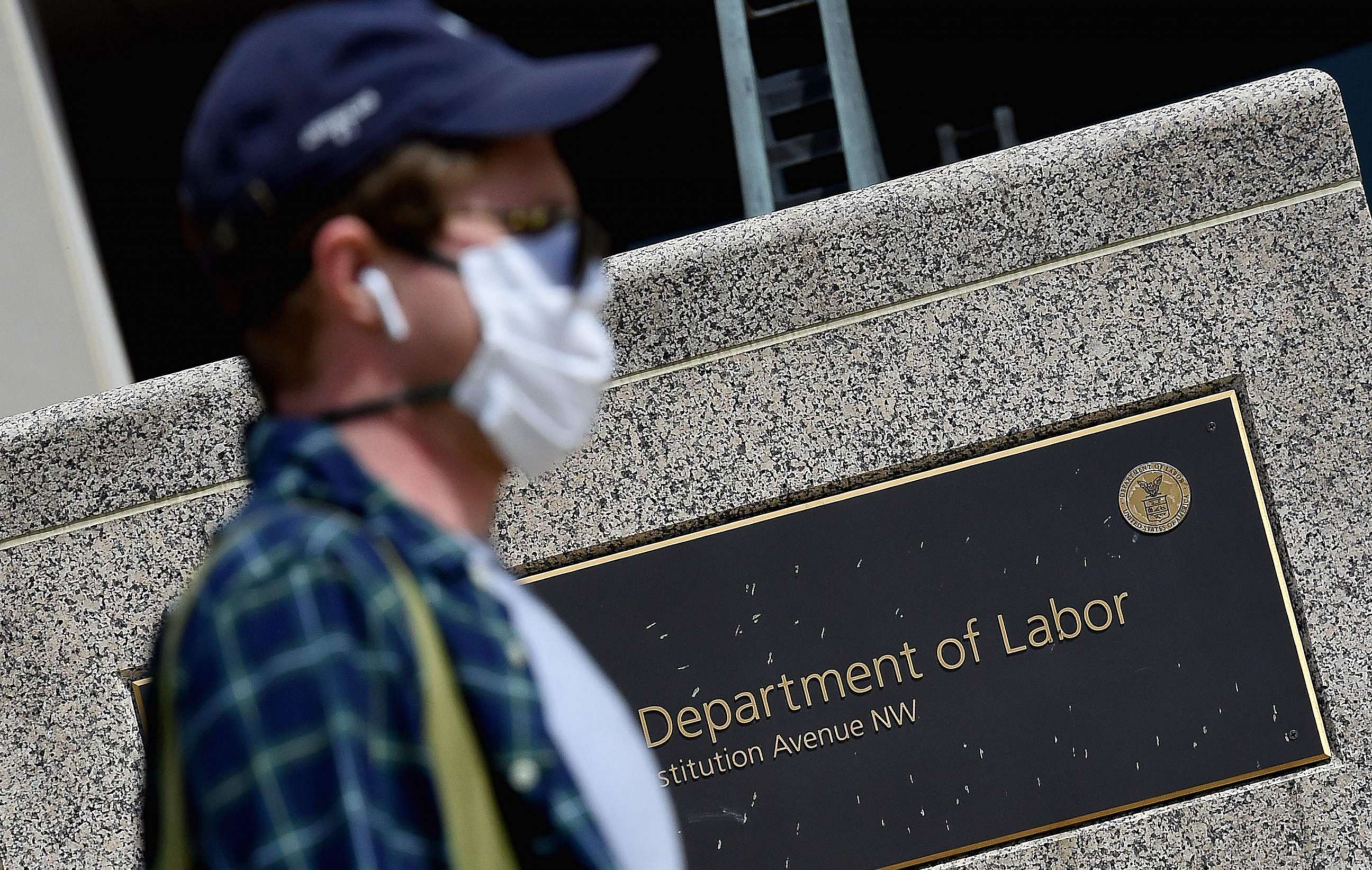 PHOTO: A woman wearing a face mask walks past a sign in front of the U.S. Department of Labor amid the coronavirus pandemic on April 29, 2020, in Washington, D.C.