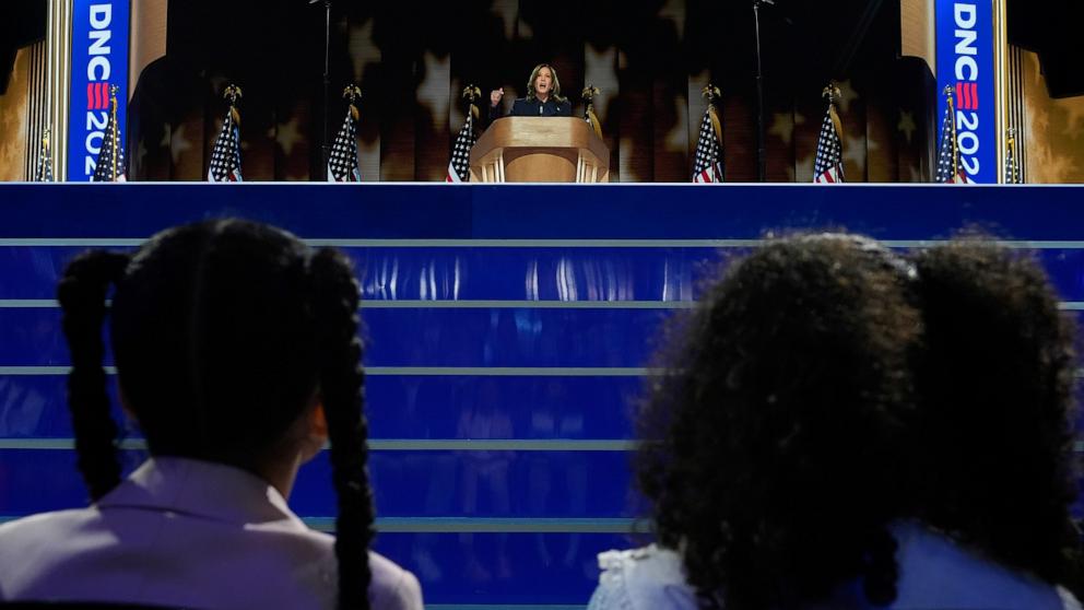 PHOTO: Democratic presidential nominee Vice President Kamala Harris speaks as her grand-nieces Amara Ajagu, left, and Leela Ajagu watch during the Democratic National Convention, Aug. 22, 2024, in Chicago.