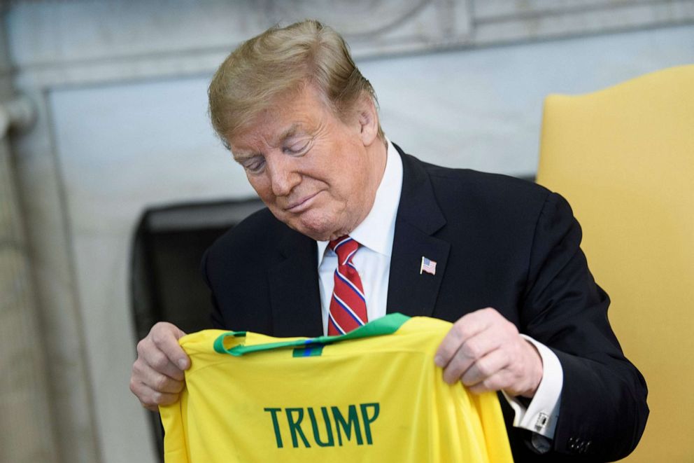 PHOTO: In this file photo taken on March 19, 2019, U.S. President Donald Trump looks at a soccer jersey given by Brazilian President Jair Bolsonaro before a meeting in the Oval Office of the White House in Washington, D.C.