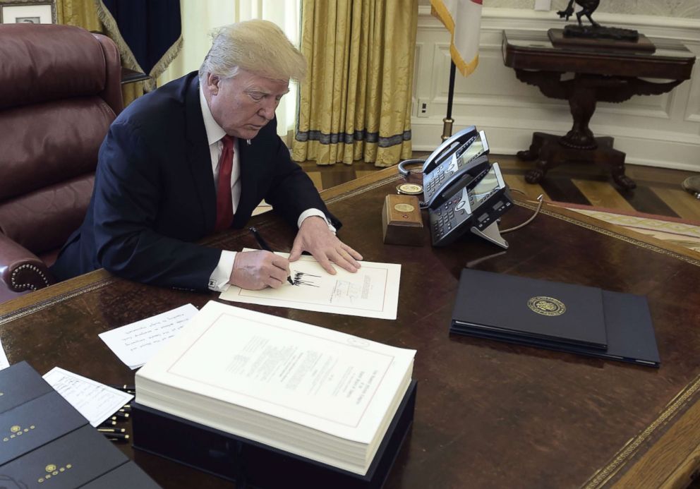   PHOTO: President Donald Trump signs a document at an event to sign the Tax Cut and Reform Bill in the Oval Office at the White House in Washington, DC, on December 22, 2017. 