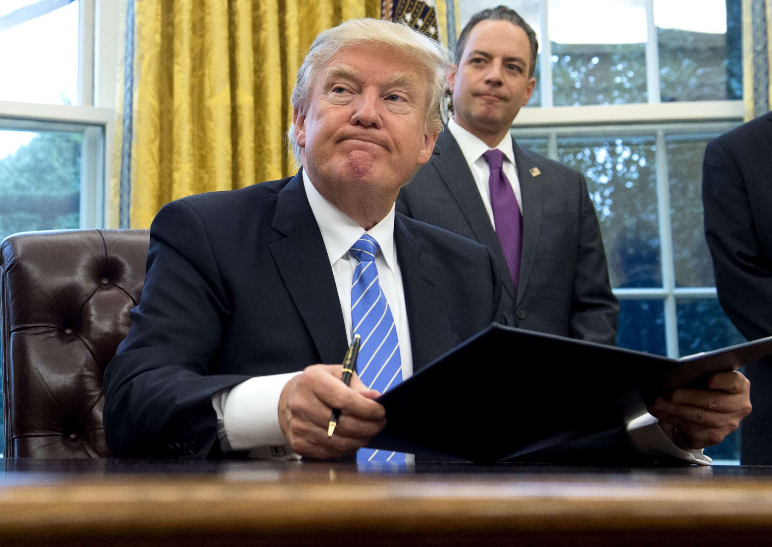 PHOTO: President Donald Trump signs an executive order as Chief of Staff Reince Priebus looks on in the Oval Office of the White House in Washington, D.C., Jan. 23, 2017.