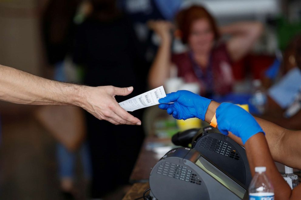 PHOTO: A poll worker hands out a voting pass to a voter for him to cast his ballot at a polling center during the Democratic presidential primary election in Miami, March 17, 2020. 