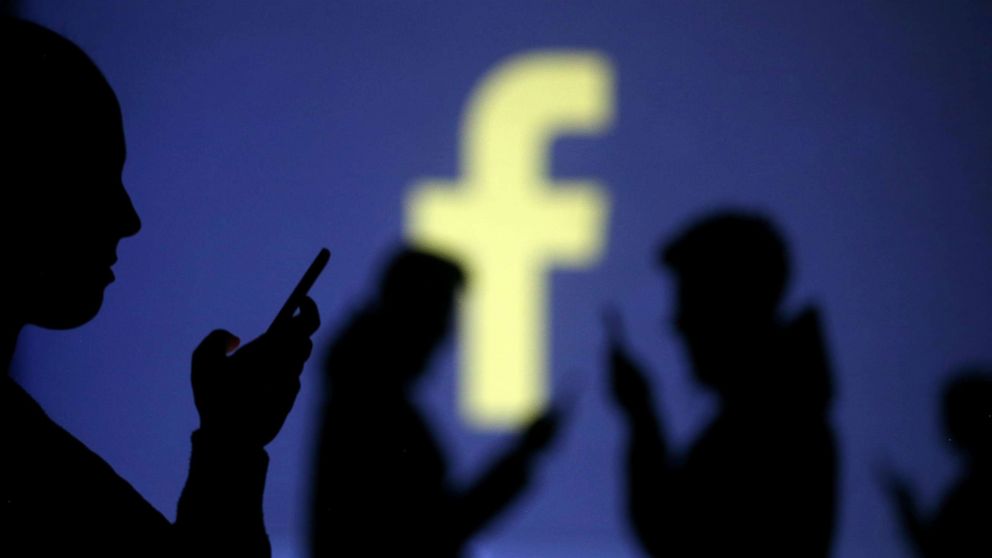 PHOTO: Silhouettes of mobile users are seen next to a screen projection of Facebook logo in this picture illustration taken March 28, 2018.