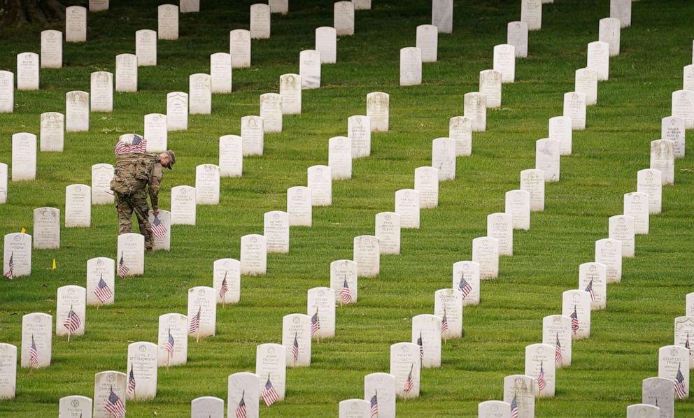 PHOTO: A soldier of the 3rd U.S. Infantry Regiment places flags on headstones ahead of Memorial Day, in Arlington, Va., May 26, 2022.