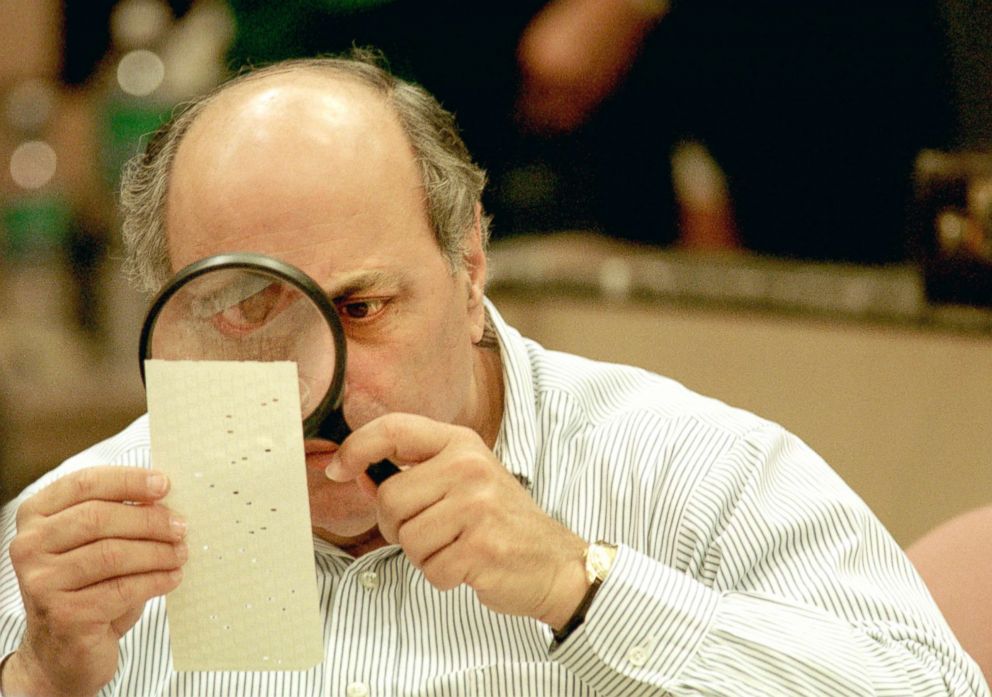 PHOTO: Judge Robert Rosenberg of the Broward County Canvassing Board uses a magnifying glass to examine a dimpled chad on a punch card ballot, Nov. 24, 2000, during a vote recount in Fort Lauderdale, Florida.