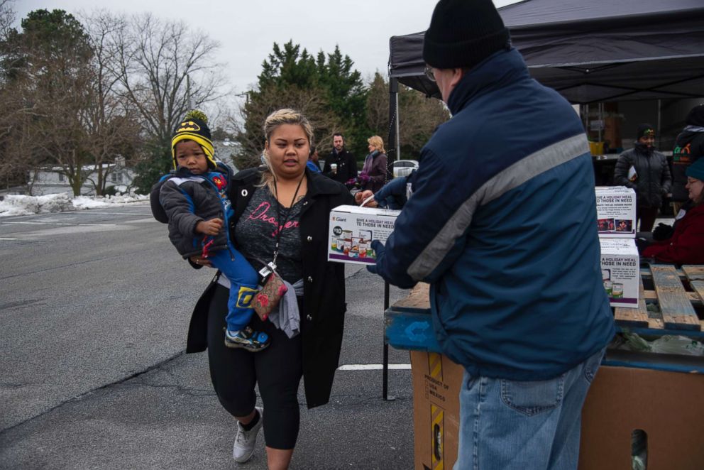 PHOTO: A State Department employee carries her son to collect food from a food bank passing out canned goods and produce to federal workers outside a Giant grocery store in Alexandra, Va., Jan. 19, 2019.