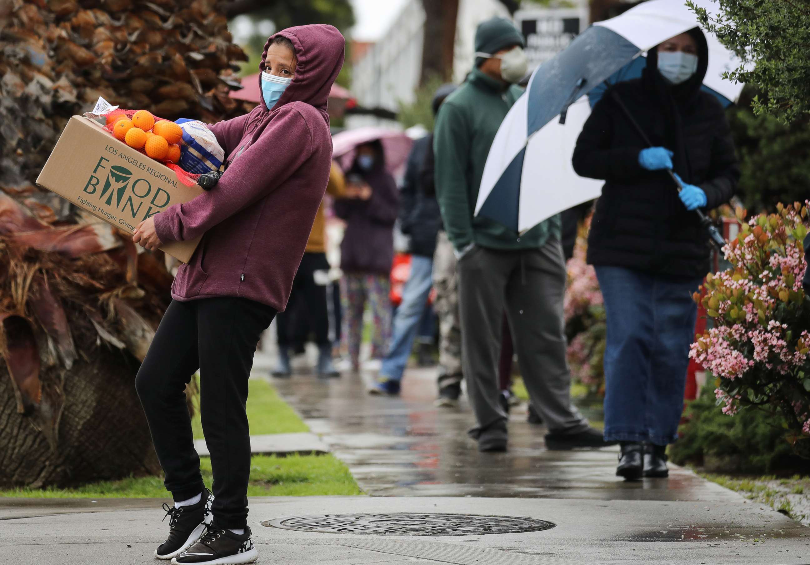 PHOTO: In this April 9, 2020, file photo, a recipient carries a box of food as others wait in line at a Food Bank distribution for those in need in Van Nuys, Calif.