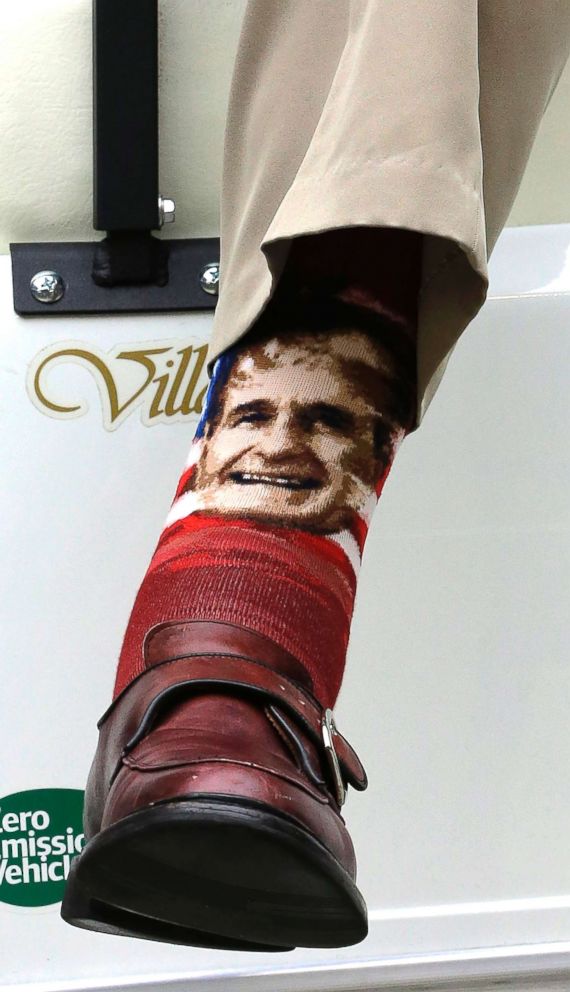 PHOTO: Former President George H.W. Bush wears socks with his image as he sits in a cart on the sidelines before an NFL football game in Houston, Dec. 1, 2013.