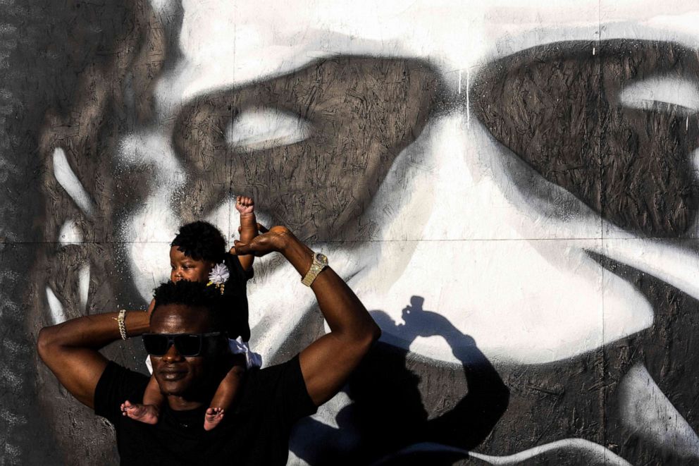 A father raises his baby daughter's fist in front of a George Floyd mural on the anniversary of George Floyd's death, at George Floyd Memorial Square in Minneapolis on May 25, 2021. 