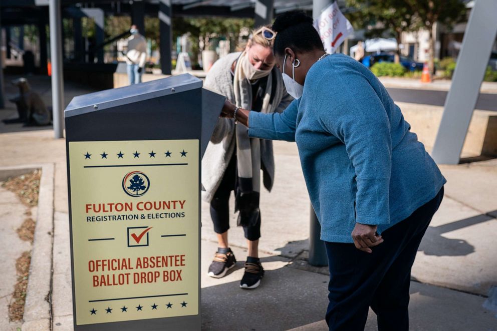 PHOTO: An election observer assists a voter as she drops off an absentee ballot into a drop box outside a polling location for the 2020 Presidential election in Atlanta, on Nov. 3, 2020.