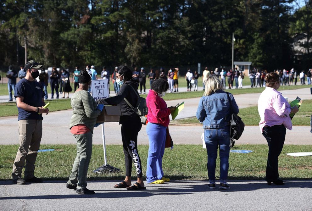 PHOTO: A poll worker hands out pens and clipboards to fill out registration cards as people stand in line to vote at the Gwinnett County Fairgrounds on Oct. 30, 2020, in Lawrenceville, Ga.