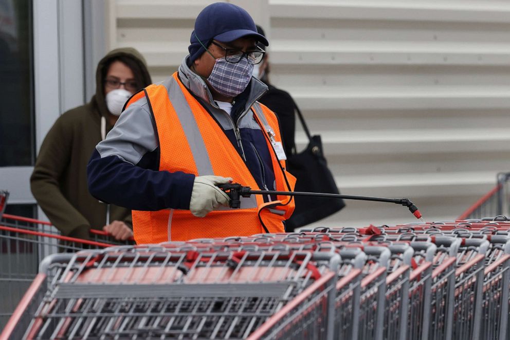 PHOTO: A Costco worker sprays disinfectant on customers' shopping carts as hundreds line up to enter the store April 16, 2020, in Wheaton, Md.