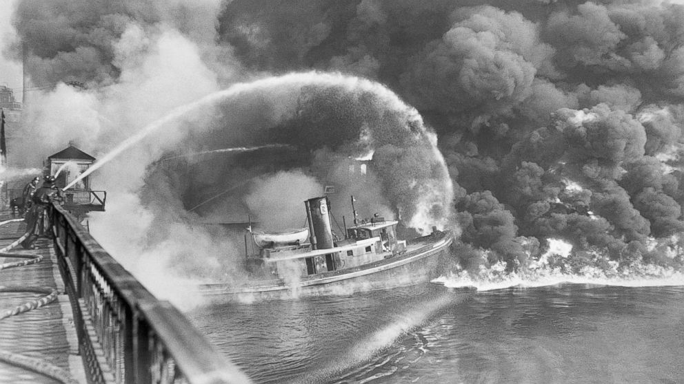 PHOTO: Firemen stand on a bridge over the Cuyahoga River to spray water on a tugboat as a fire burns an oil slick on the river, Nov. 3, 1952.

