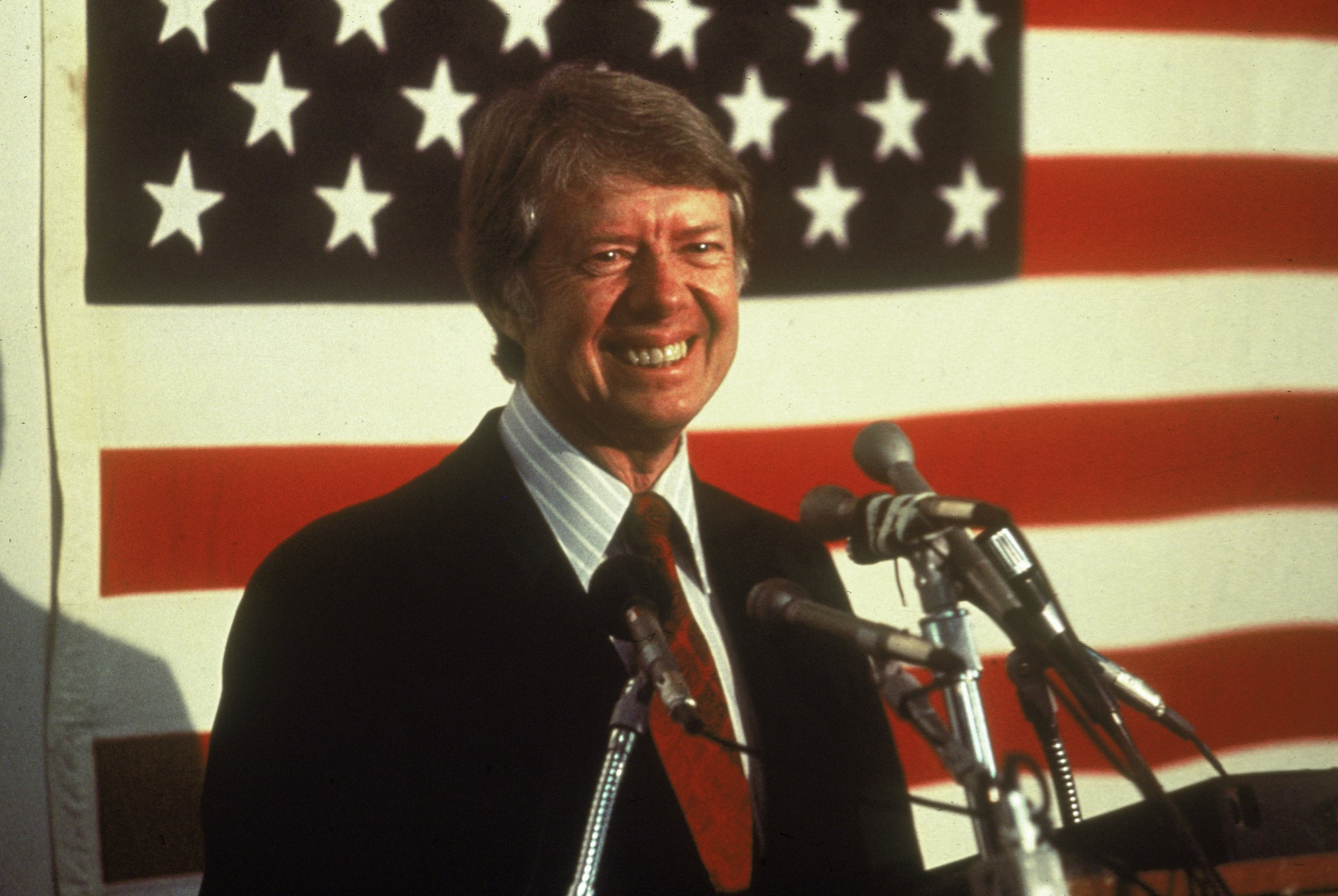 PHOTO: U.S. President Jimmy Carter smiling at a podium in front of an American flag. 