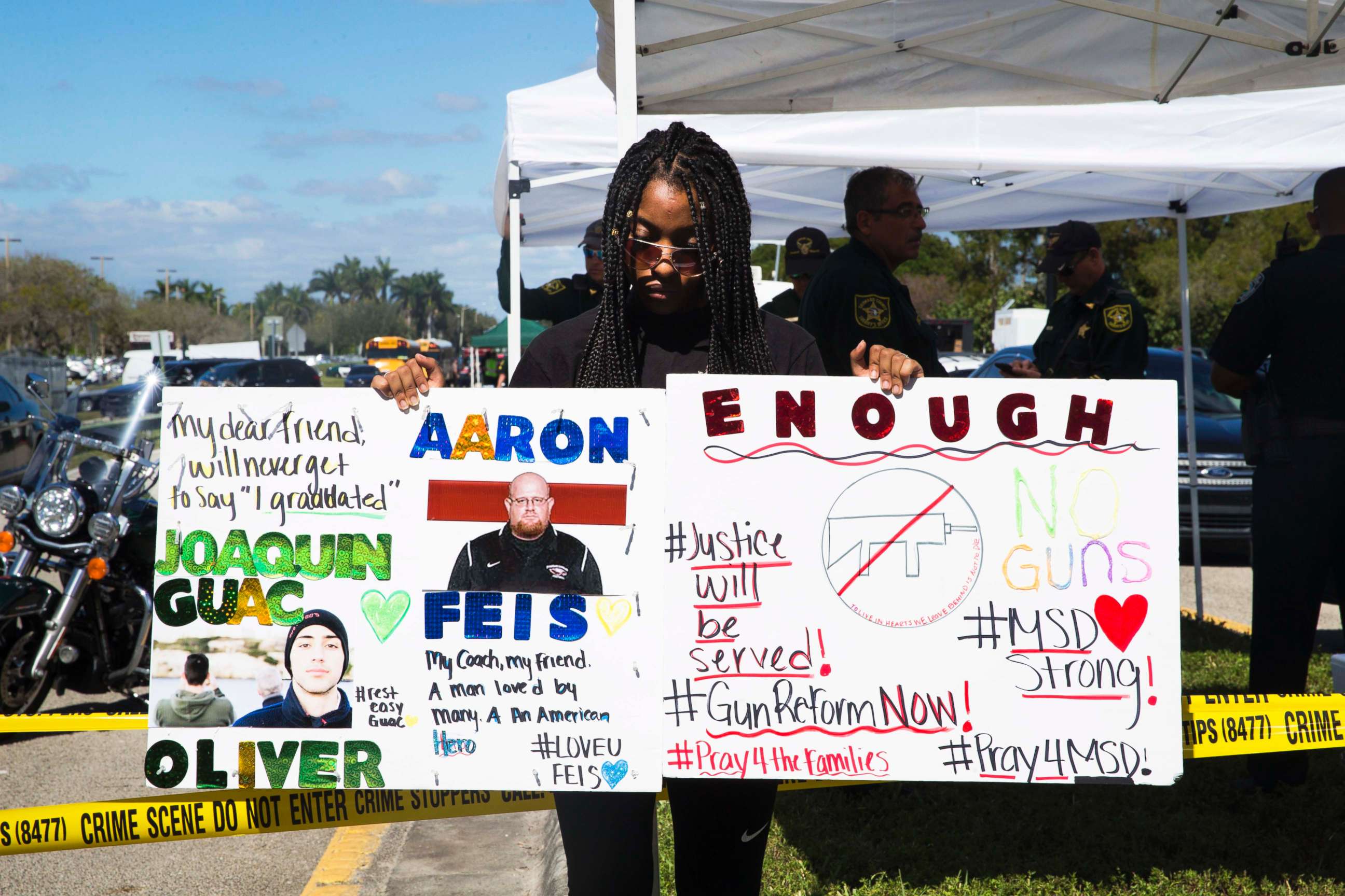 PHOTO: Tyra Hemats, 19, a 12th grader at Marjory Stoneman Douglas High School, stands with signs, one advocating for gun reform and another honoring her coach and friend, both of whom were killed in Wednesday's shooting, on Feb. 15, 2018. 