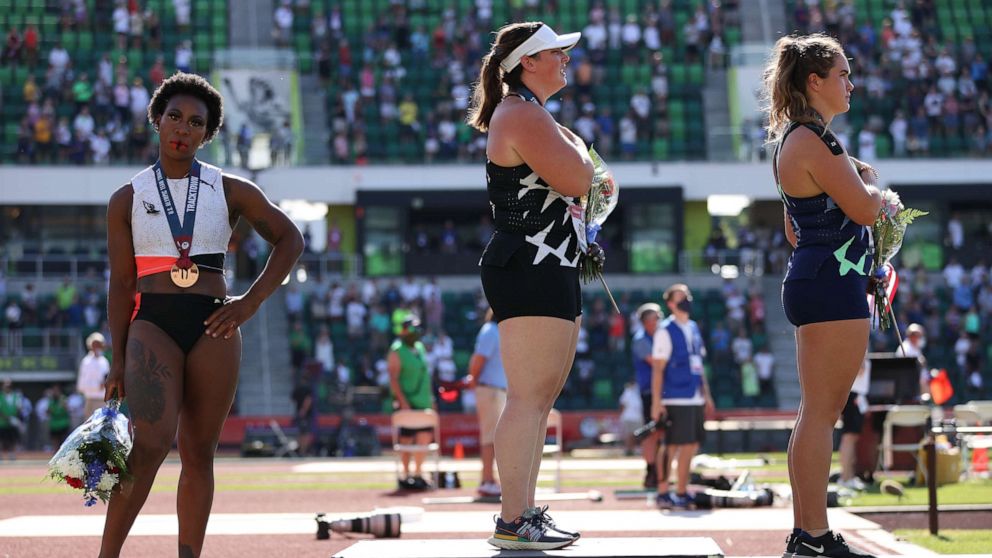 PHOTO: Gwendolyn Berry turns away from U.S. flag as DeAnna Price and Brooke Andersen stand on the podium after the Women's Hammer Throw final on day nine of the 2020 U.S. Olympic Track & Field Team Trials at Hayward Field on June 26, 2021, in Eugene, Ore.