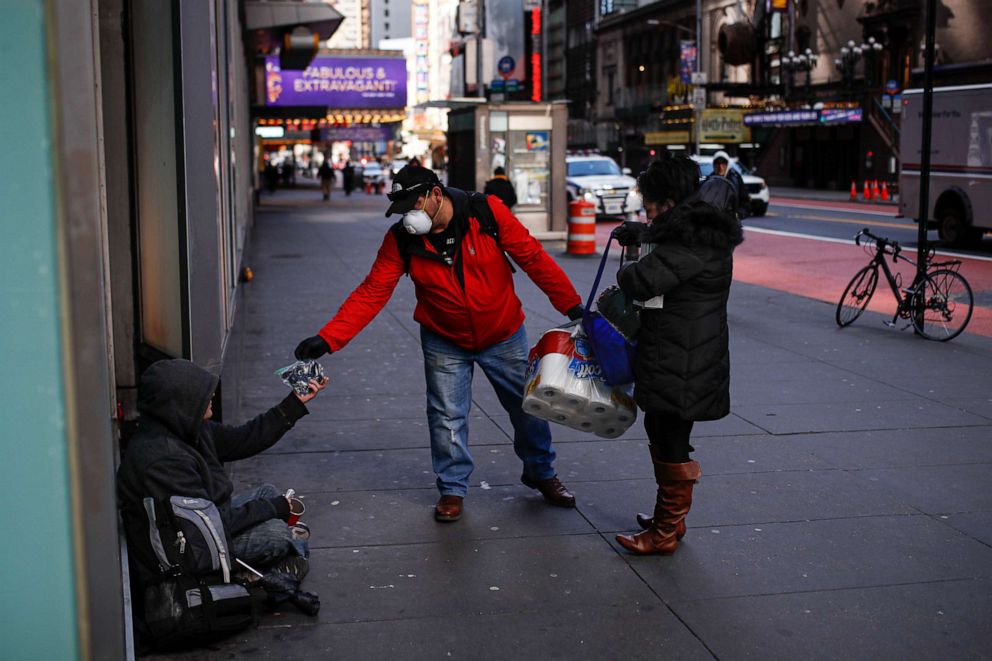 PHOTO: Virna Munoz-Guzman, 52, right, and her husband Felix, wear protective gloves and masks due to COVID-19 concerns as they hand out disposable gloves and sanitizing wipes to people who are homeless on 42nd Street, March 21, 2020, in New York.