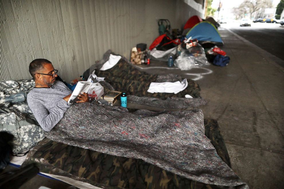 PHOTO: Travis Stanley, who said he has been homeless for three months and is a U.S. Navy veteran, reads on donated bedding where he normally sleeps beneath an overpass on June 5, 2019, in Los Angeles.