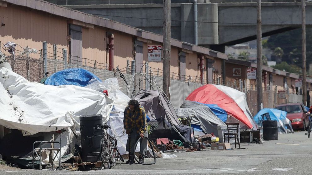 PHOTO: This Thursday, June 27, 2019, file photo shows a man holding a bicycle tire outside of a tent along a street in San Francisco.