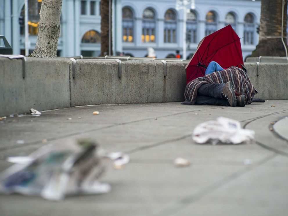 PHOTO: A man lies under a blanket by an umbrella in Justin Herman Plaza in San Francisco, Jan. 21, 2016.