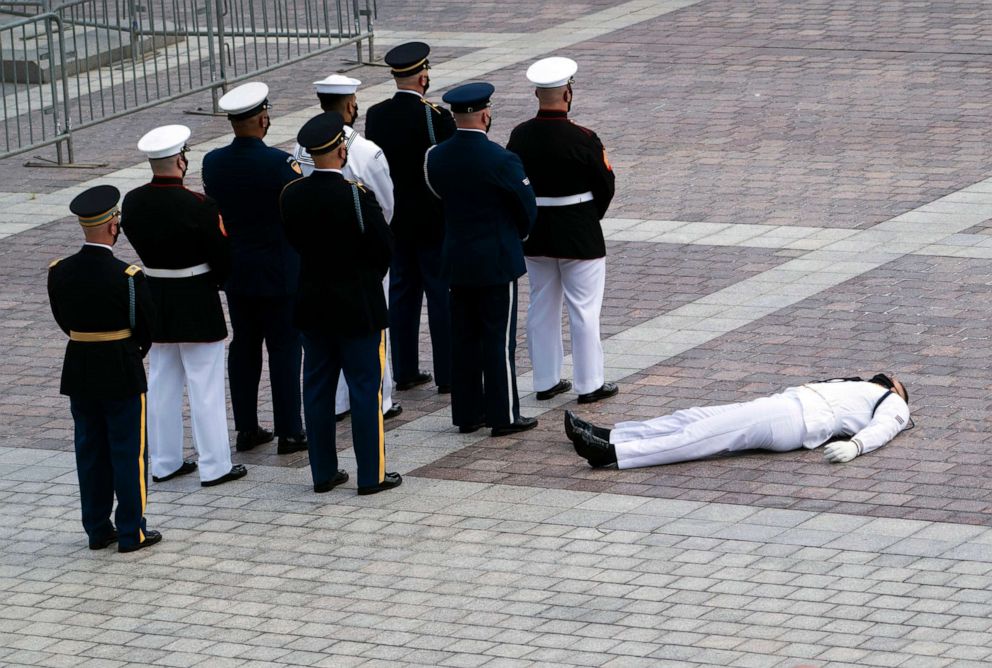 PHOTO: A member of the joint services military honor guard lies on the ground after collapsing in the heat before carrying the flag-draped casket of Rep. John Lewis, D-Ga., at the Capitol, July 27, 2020.