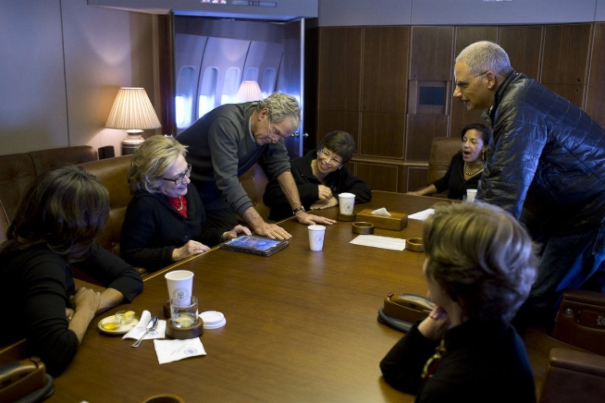 On Air Force One, former President Bush shows photos to First Lady Michelle Obama, former Secretary of State Hillary Clinton, Valerie Jarrett, National Security Advisor Susan E. Rice, Attorney General Eric Holder and former First Lady Laura Bush.