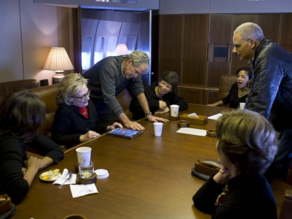 On Air Force One, former President Bush shows photos to First Lady Michelle Obama, former Secretary of State Hillary Clinton, Valerie Jarrett, National Security Advisor Susan E. Rice, Attorney General Eric Holder and former First Lady Laura Bush.