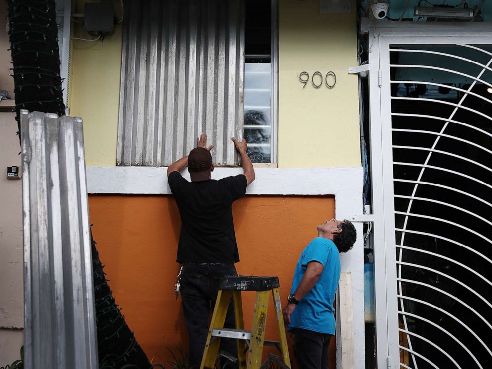 PHOTO: Workers place hurricane shutters over a window as they help prepare a business for the possible arrival of Hurricane Dorian on Aug. 30, 2019, in Miami Beach, Fla.