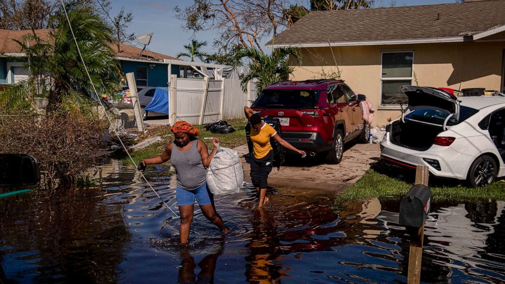 PHOTO: Atlas Dorlean, left, carries a bag of salvaged belongings through floodwater left after Hurricane Ian tore through the Harlem Heights area of Fort Myers, Fla. Sept. 29, 2022.