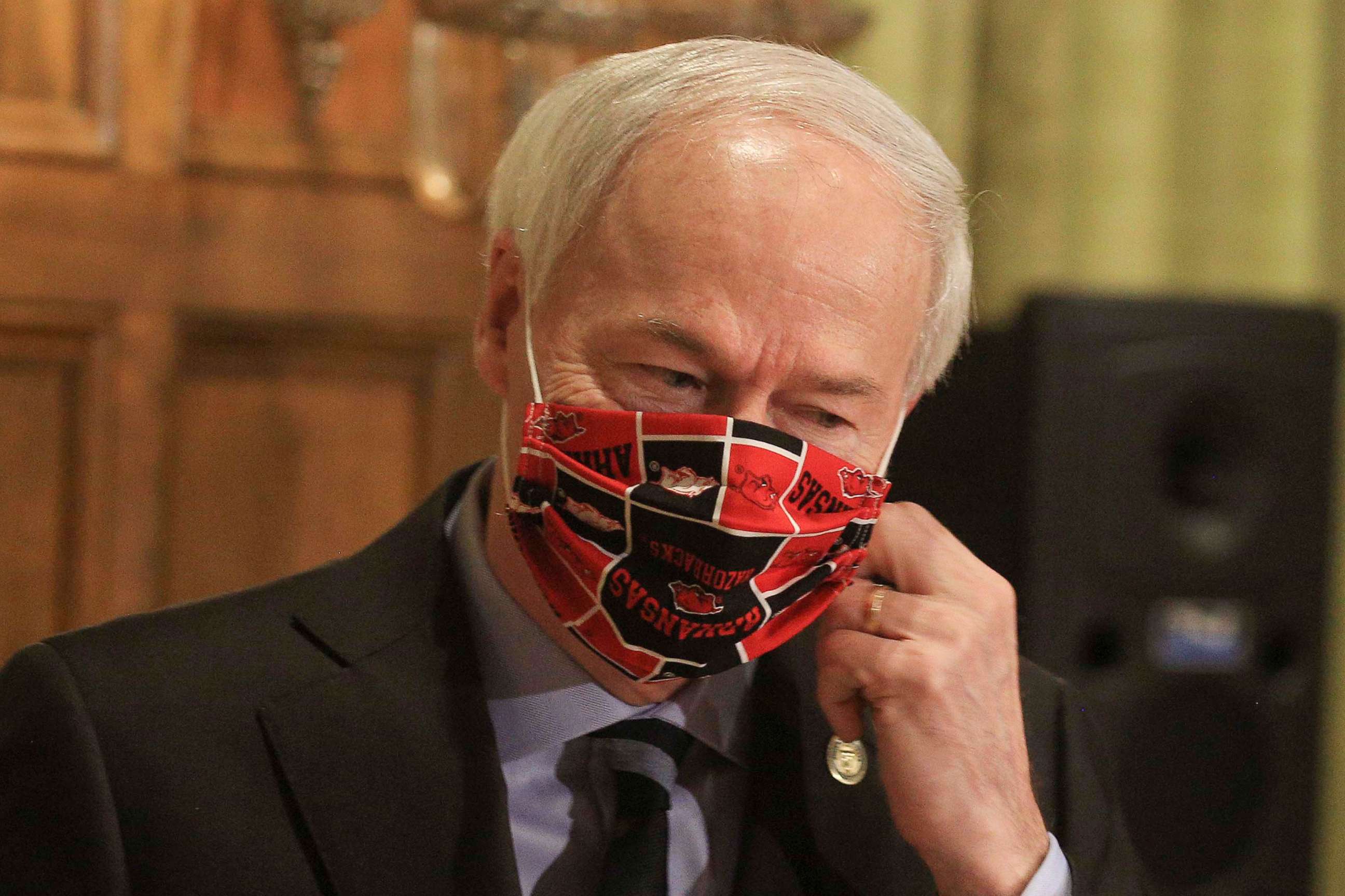 PHOTO: In this Monday, April 27, 2020 photo, Gov. Asa Hutchinson takes off his Arkansas Razorbacks facemark as he arrives for the daily coronavirus briefing at the state Capitol in Little Rock.