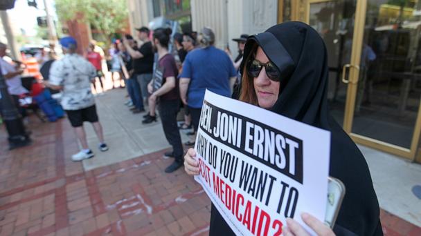 DAVENPORT, IOWA- JUNE 23:  Lesa Hadley of Bettendorf, Iowa stands  outside the office of U.S. Sen. Joni Ernst (R-IA) wearing a cloak as part of a mock funeral to protest against proposed Medicaid cuts on June 23, 2025  in Davenport, Iowa.