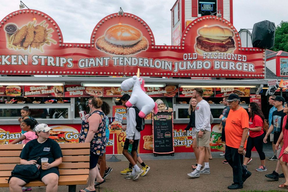 PHOTO: People walk past a food stand at the Iowa State Fair, Aug. 11, 2019, in Des Moines, Iowa.