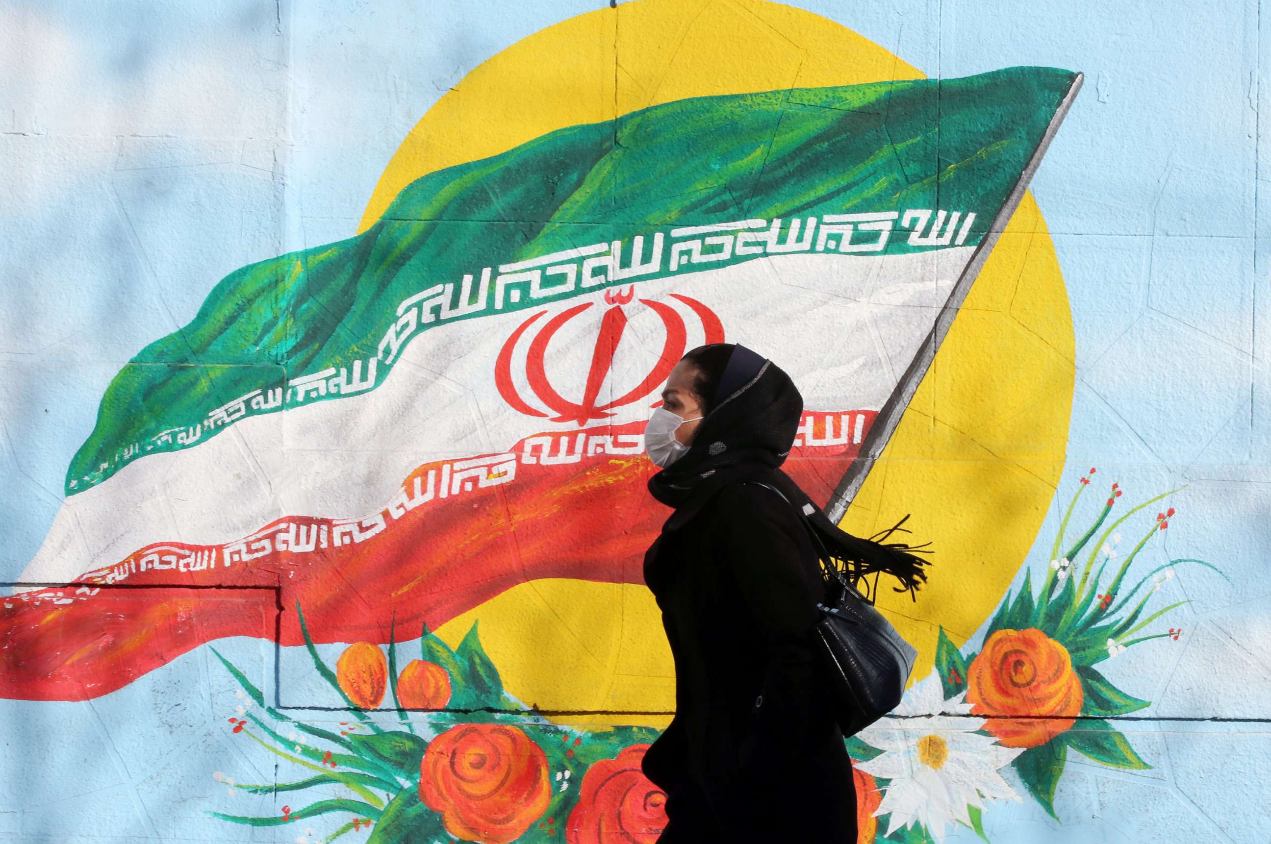 PHOTO:An Iranian woman wearing a mask walks next to a wall painting of Iranian national flag in Tehran, Iran, Feb. 12, 2020.