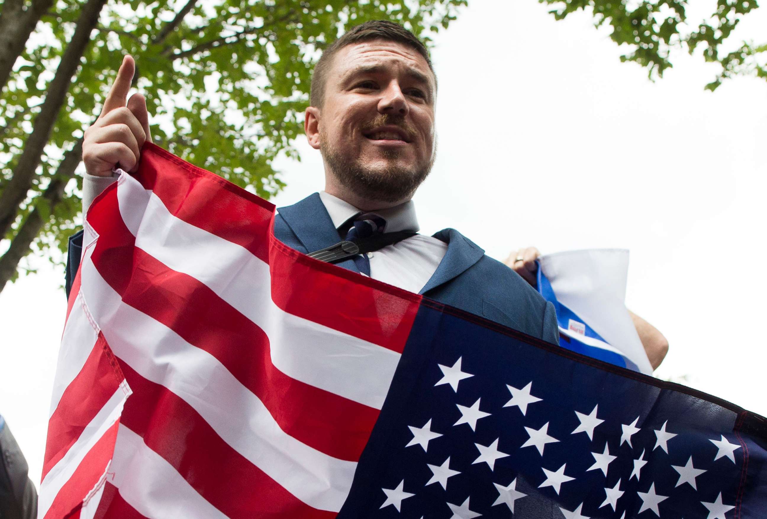 PHOTO: Jason Kessler speaks to members of the news media while holding a U.S. national flag in Lafayette Park across the street from the White House, during the "Unite the Right" rally, Aug. 12, 2018.