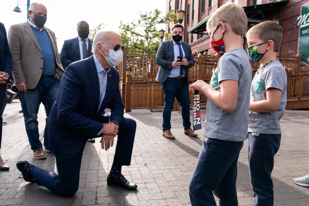 PHOTO: Democratic presidential candidate former Vice President Joe Biden, joined by Duluth Mayor Emily Larson, left and Minnesota Gov. Tim Walz, takes a knee to talk with twin brothers as he arrives at Amazing Grace Bakery & Cafe Friday, Sept. 18, 2020.